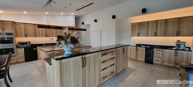 Modern kitchen featuring natural hickory cabinetry with black granite countertops, a large central island, stainless steel appliances, and ambient lighting. Project by Interstate Custom Kitchen & Bath, Inc.