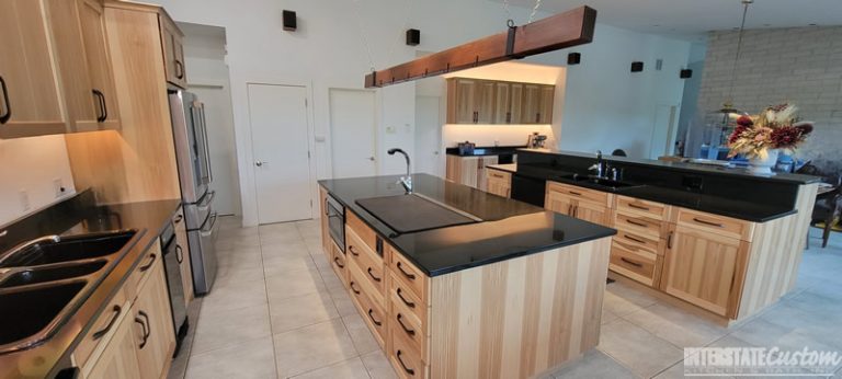 Modern kitchen with natural hickory cabinetry, black countertops, a large central island with a sink, and stainless steel appliances, showcasing an open layout. Project by Interstate Custom Kitchen & Bath, Inc.