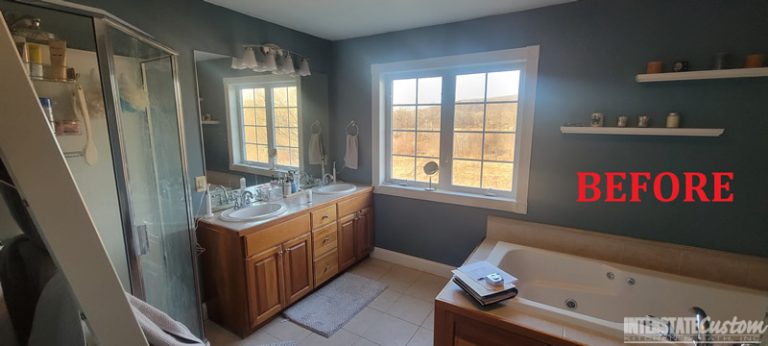 Before image of a bathroom featuring a double vanity with wood cabinetry and a large mirror, a spacious bathtub, and a glass-enclosed shower. The room has dark blue walls, white trim around the window, and beige tile flooring