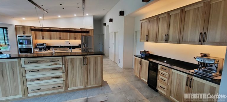 Modern kitchen with natural hickory cabinetry, black granite countertops, a large central island, stainless steel appliances, and ambient lighting. Project by Interstate Custom Kitchen & Bath, Inc.