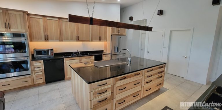 Modern kitchen with cabinet refacing featuring light wood cabinetry, black countertops, a large central island with a sink, and stainless steel appliances. Project by Interstate Custom Kitchen & Bath, Inc.