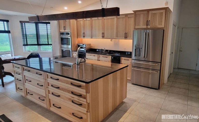 After image of a kitchen with light wood cabinetry, black countertops, a large central island with a sink, and stainless steel appliances, showcasing the results of cabinet refacing. Project by Interstate Custom Kitchen & Bath, Inc.