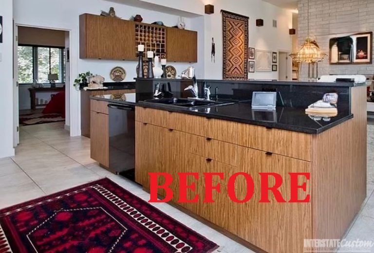 Before image of a kitchen with dark wood cabinetry, black countertops, and a central island with a sink, featuring a traditional rug and decorative wall hangings. Project by Interstate Custom Kitchen & Bath, Inc