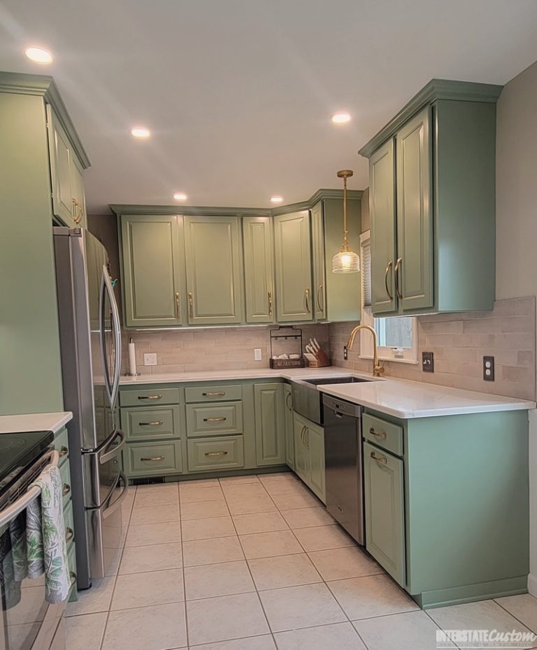 Completed kitchen refacing project with green cabinetry, stainless steel appliances, white countertops, and a tiled backsplash, featuring a farmhouse sink and gold fixtures. Project by Interstate Custom Kitchen & Bath, Inc.