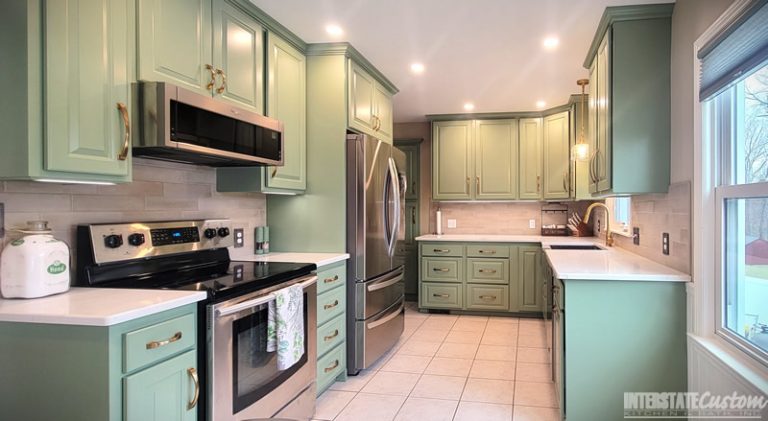 Completed kitchen refacing project with green cabinetry, stainless steel appliances, white countertops, and a tiled backsplash. Project by Interstate Custom Kitchen & Bath, Inc
