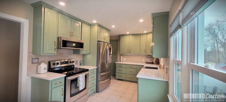 Completed kitchen refacing project with green cabinetry, stainless steel appliances, white countertops, and a tiled backsplash, offering a bright and airy atmosphere. Project by Interstate Custom Kitchen & Bath, Inc.