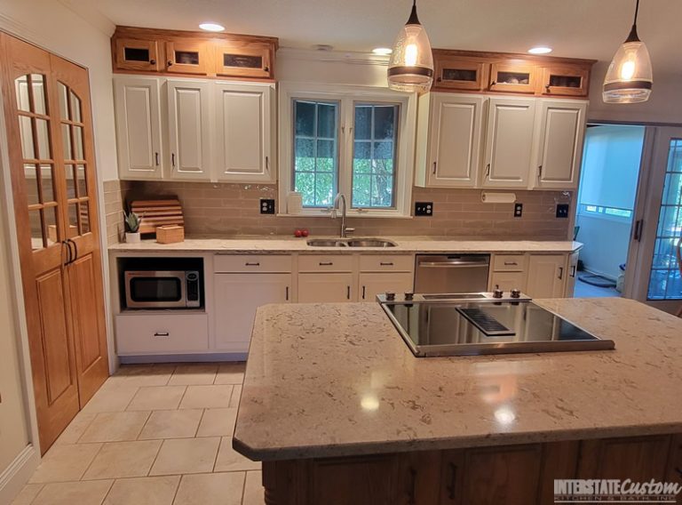 Kitchen cabinet refacing project with white cabinetry, a beige tiled backsplash, light countertops, and modern pendant lighting. Project by Interstate Custom Kitchen & Bath, Inc