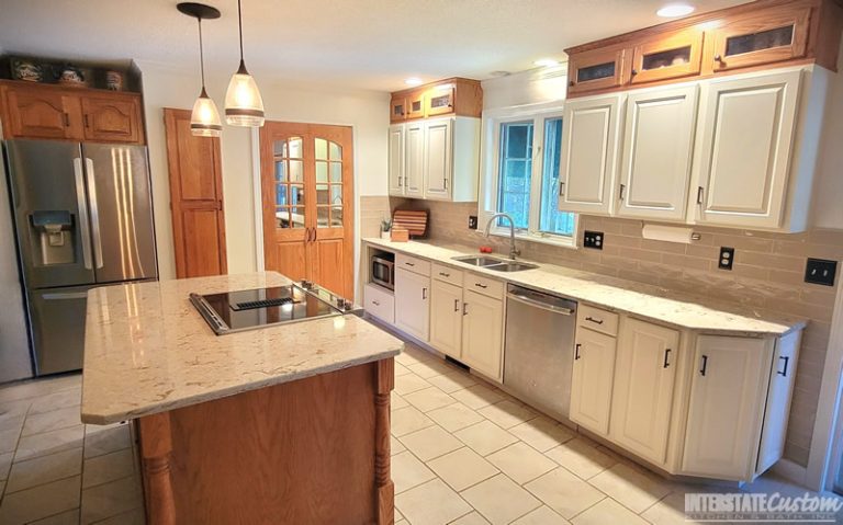 Kitchen cabinet refacing project with white cabinetry, a beige tiled backsplash, light countertops, and modern pendant lighting. Project by Interstate Custom Kitchen & Bath, Inc.