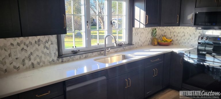 Hanstone Chantilly lace quartz countertops with a stainless steel sink and natural marble braided mosaic tile backsplash in the Simply Elegant kitchen remodel. Project by Interstate Custom Kitchen & Bath, Inc.