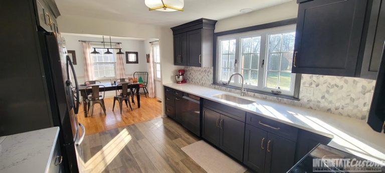 Another angle of the Simply Elegant kitchen remodel showcasing North Point cabinetry window over sink in a shaker style maple slate door, Hanstone Chantilly lace quartz countertops, and natural marble braided mosaic tile backsplash. Project by Interstate Custom Kitchen & Bath, Inc.