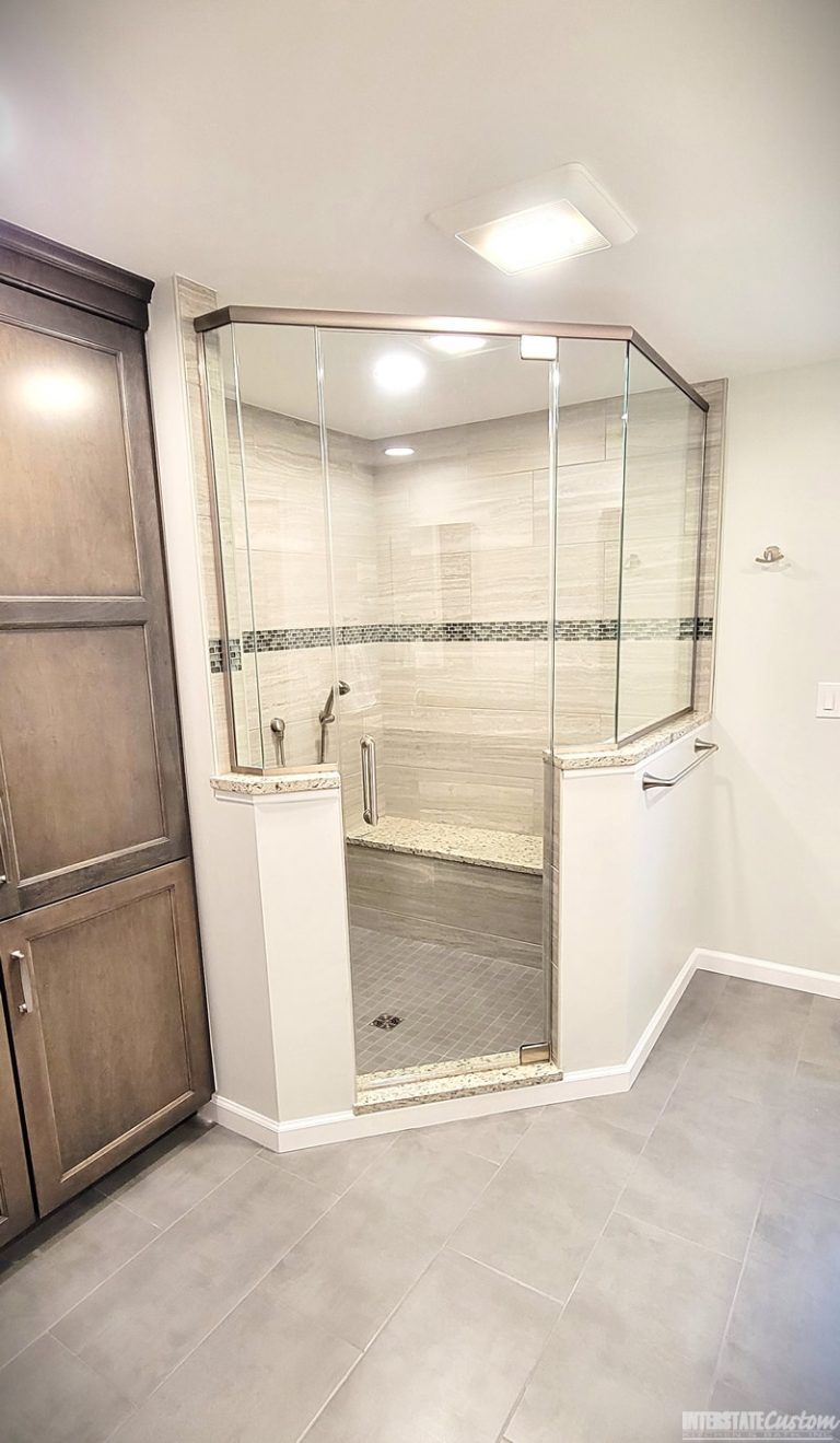 Modern bathroom featuring a large walk-in shower with frameless glass doors, tiled walls with a decorative mosaic band, granite surfaces, and ample cabinet storage.