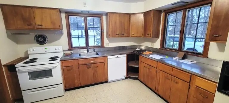 Outdated kitchen with wood cabinets, laminate countertops, electric stove, and window-lined walls