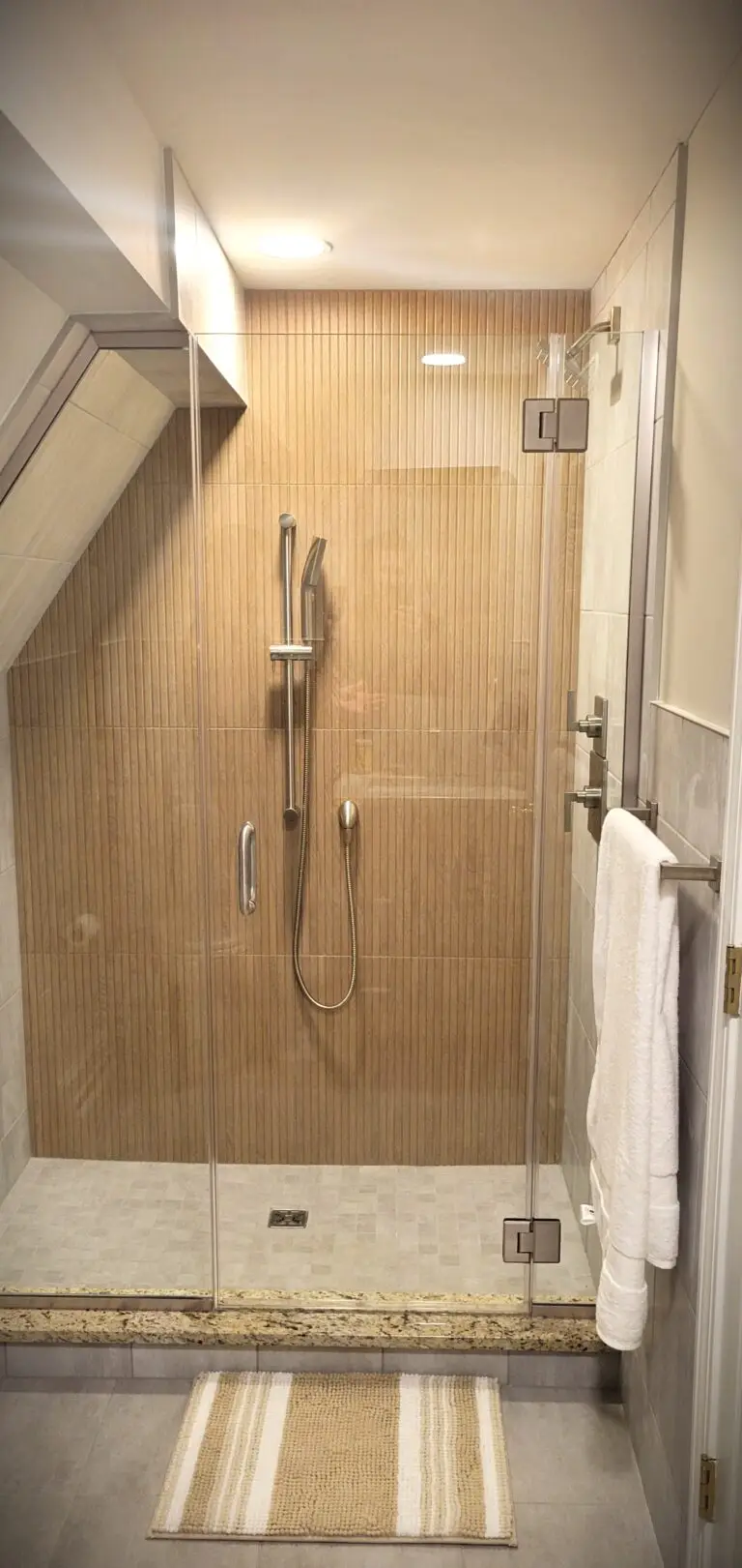 Modern bathroom remodel with glass shower enclosure, tile walls, and sloped ceiling design