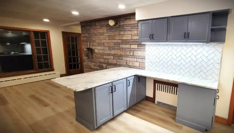 Close-up of kitchen corner with quartz countertop, gray cabinets, and white herringbone tile backsplash